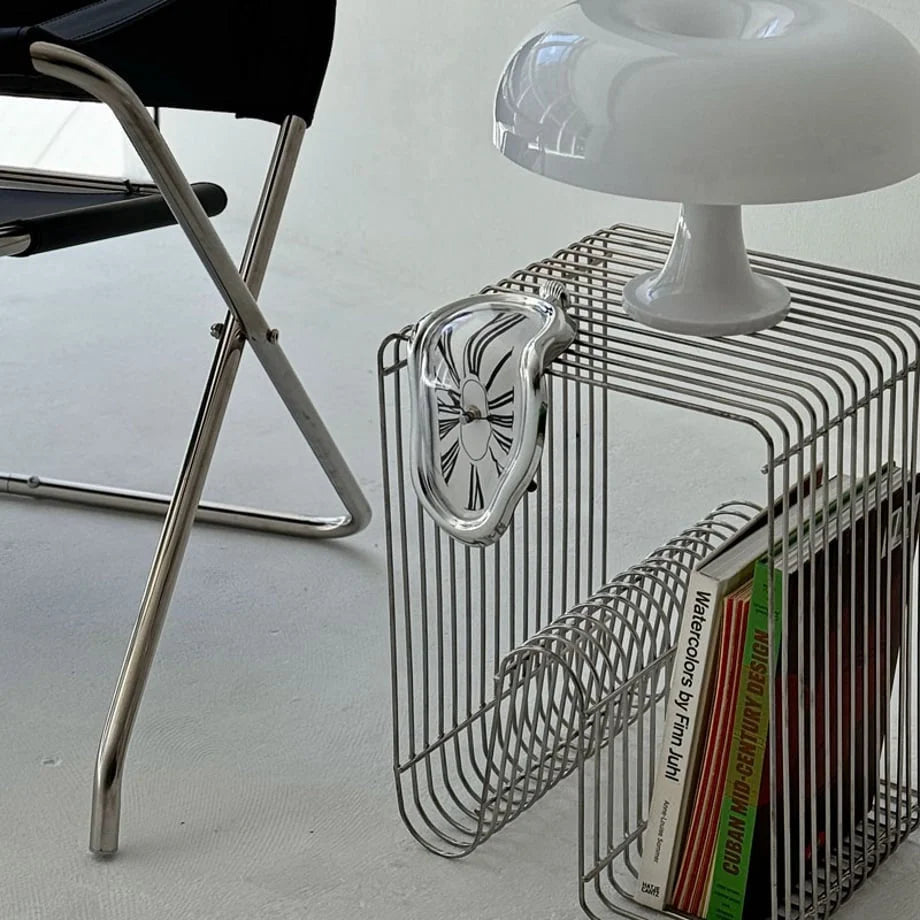 Silver Surrealist Melting Clock hanging from a chrome wire side table next to a mushroom lamp.