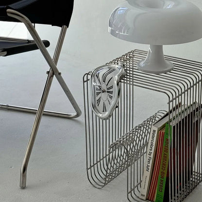Silver Surrealist Melting Clock hanging from a chrome wire side table next to a mushroom lamp.