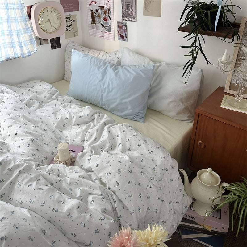 White cotton bedding with tiny blue flowers, green leaves and scattered dots, styled with a pale blue pillow - Roomden