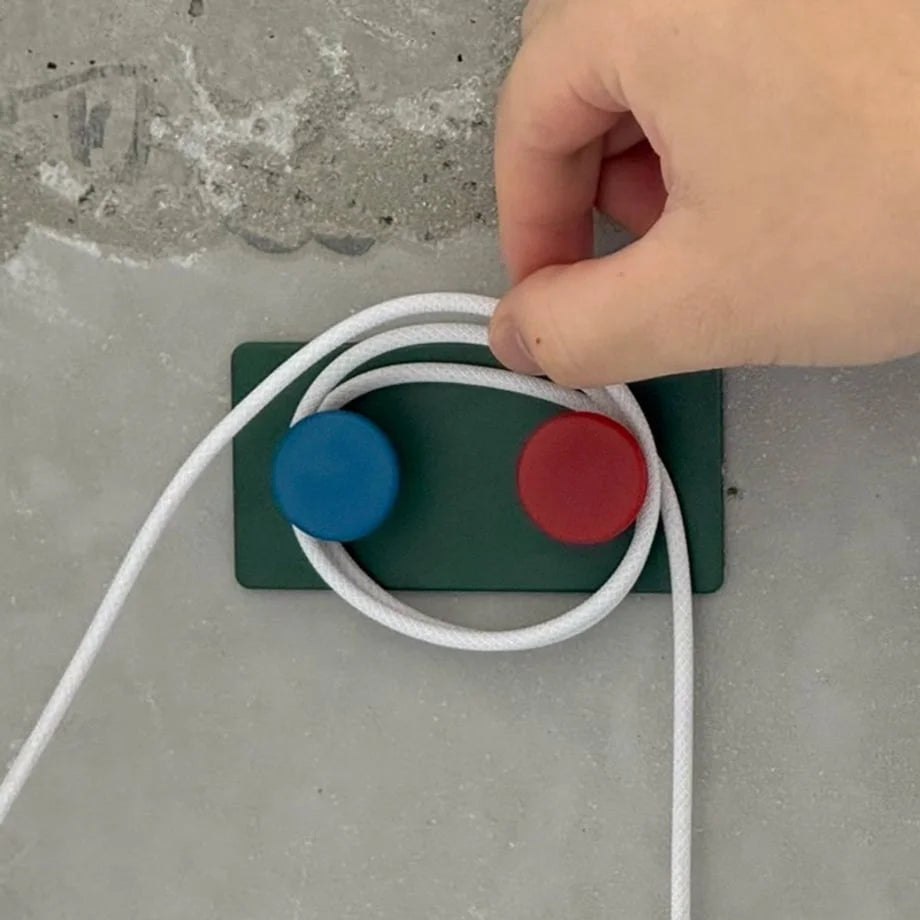 A hand wrapping a white cable around the Green Colorblock Decorative Hook, showing its use as a cord winder - RoomDen.