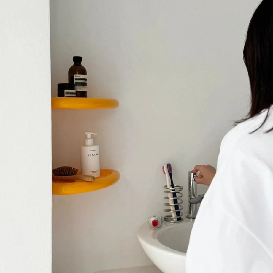A person in a white shirt admiring two yellow corner shelves in a bright, modern bathroom setting. - RoomDen