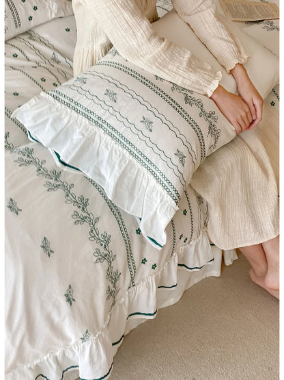 A person resting on the bed, showing a close-up of the Forest Green embroidered and ruffled pillow sham.