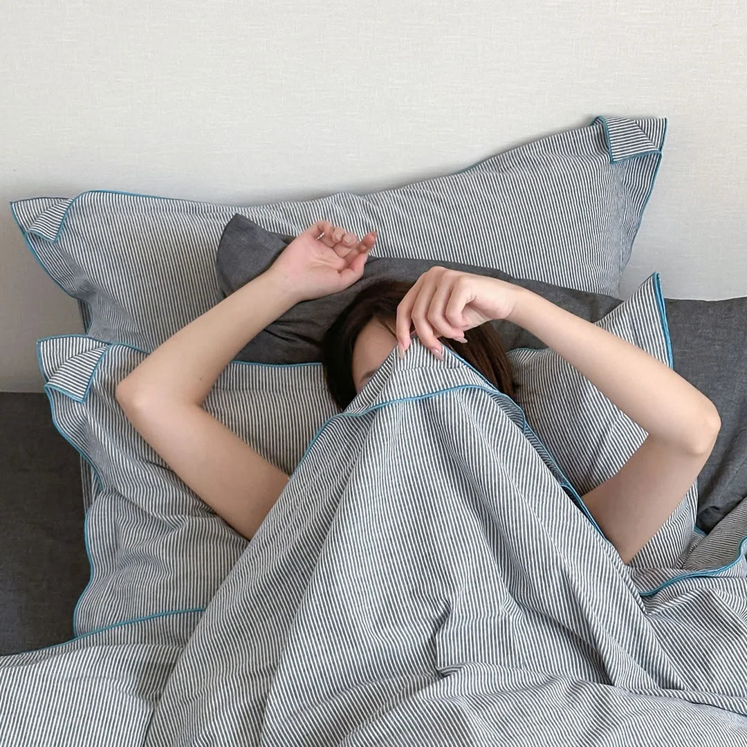 A person playfully hiding under the Dark Grey & Blue Pinstripe Washed Cotton Duvet Cover.