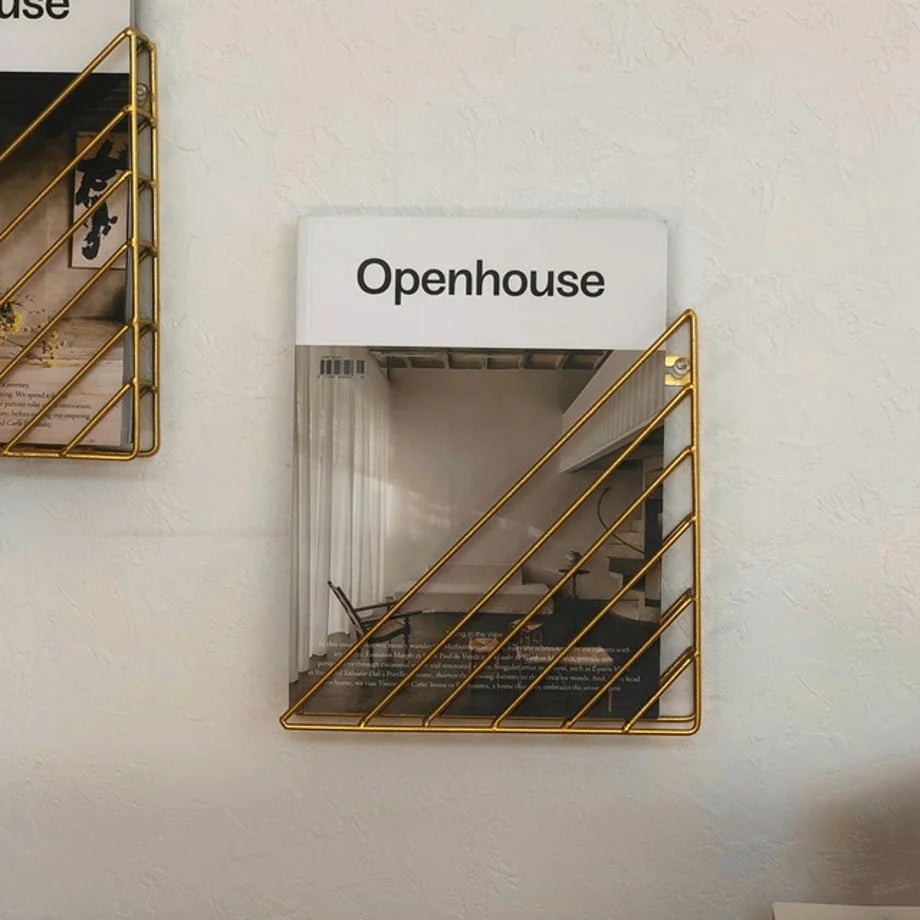 Close-up of the gold metal wireframe magazine holder mounted on a textured wall - RoomDen