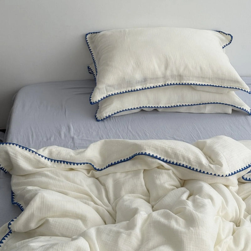 Cream white washed cotton bedding set with blue embroidered edge on a bed with a light blue sheet.