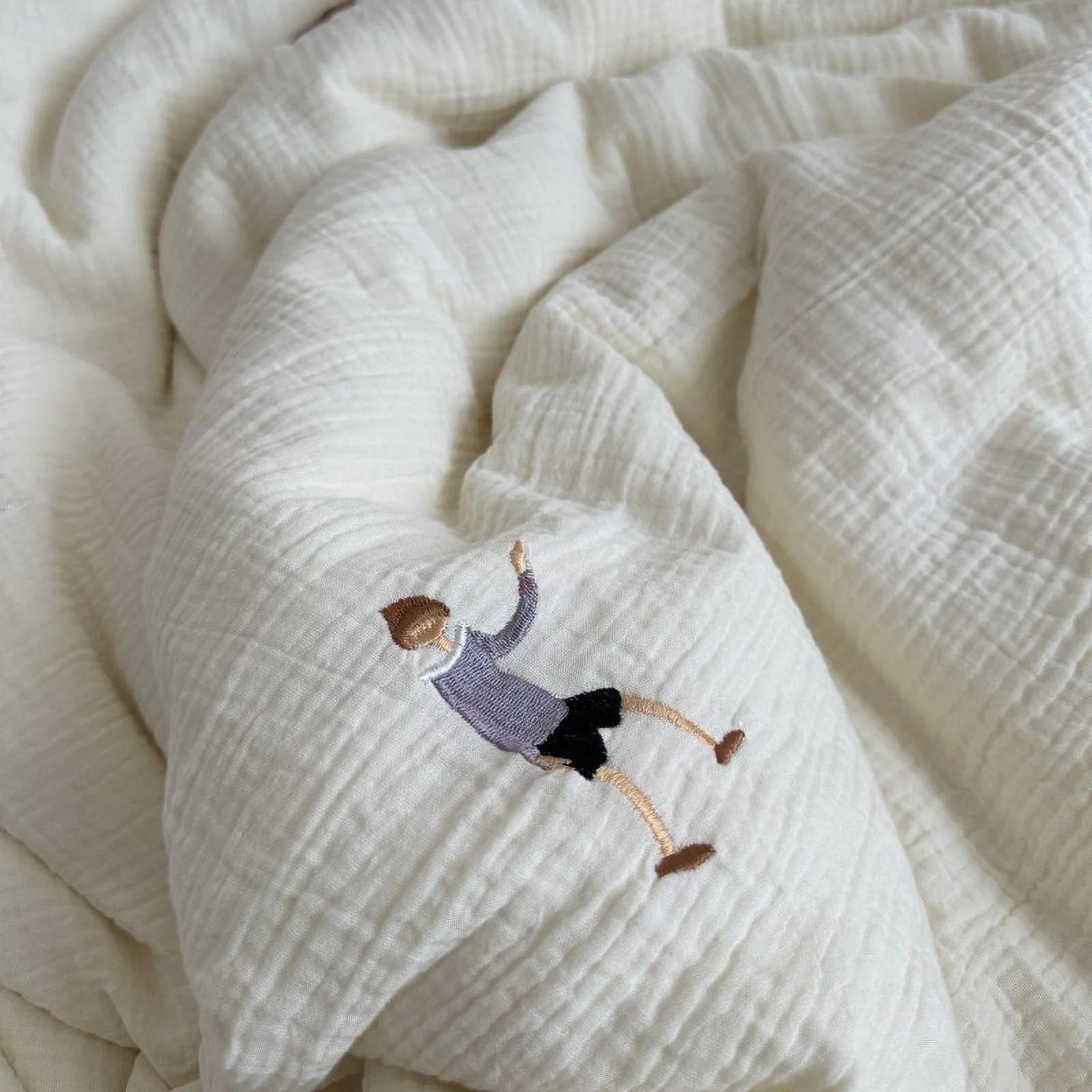 Detail shot of the crinkled washed cotton fabric, highlighting an embroidered character of a person falling.