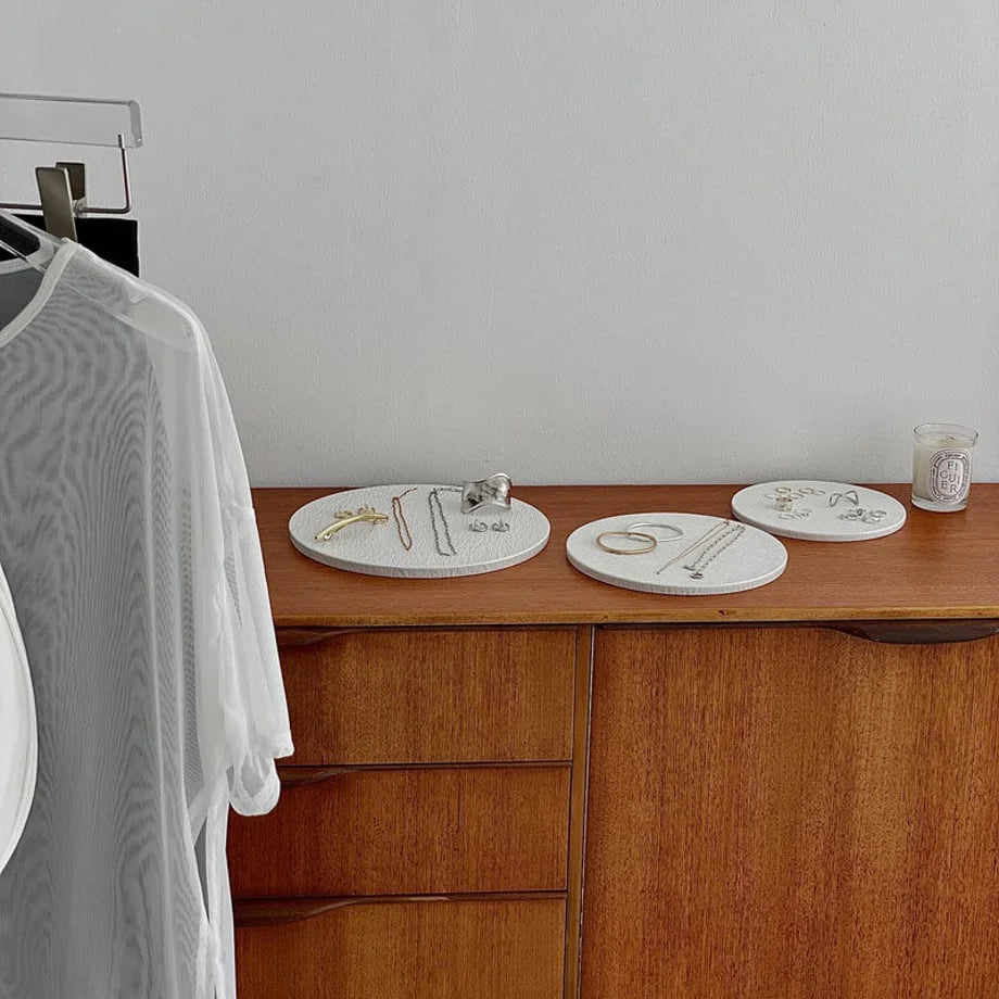 Wide view of the textured ceramic jewelry trays on a dresser next to a candle and a white mesh top on a hanger. - RoomDen