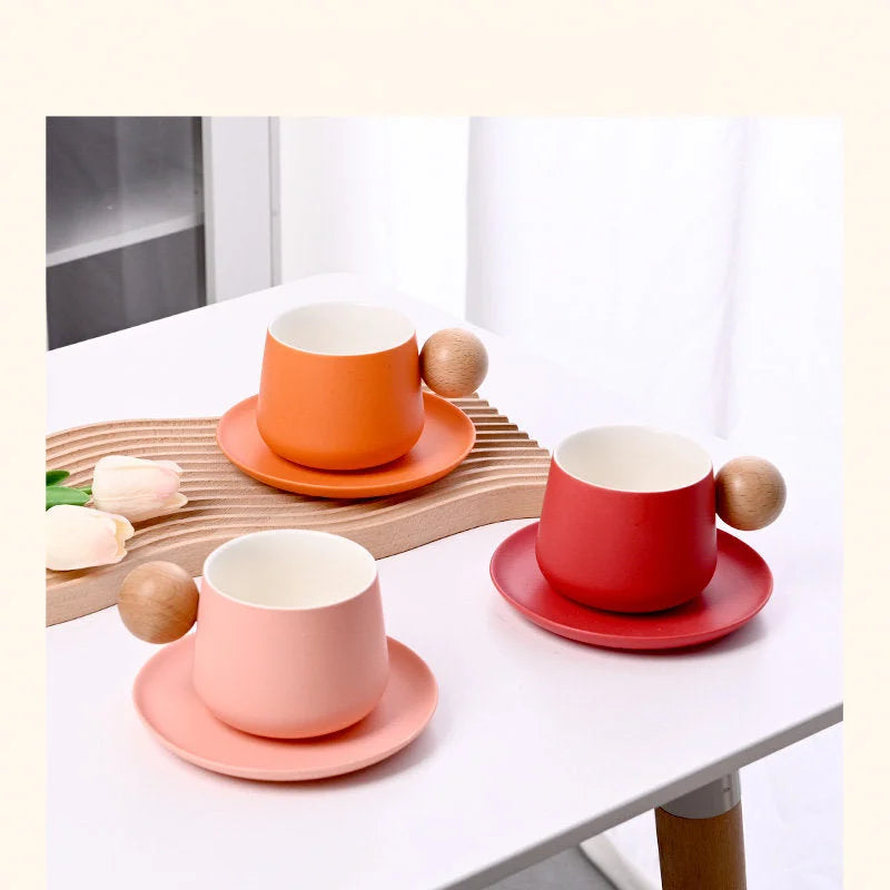 Three Frosted Ceramic Mug Sets in Orange, Red, and Pink with wooden ball handles, arranged on a white table. - RoomDen