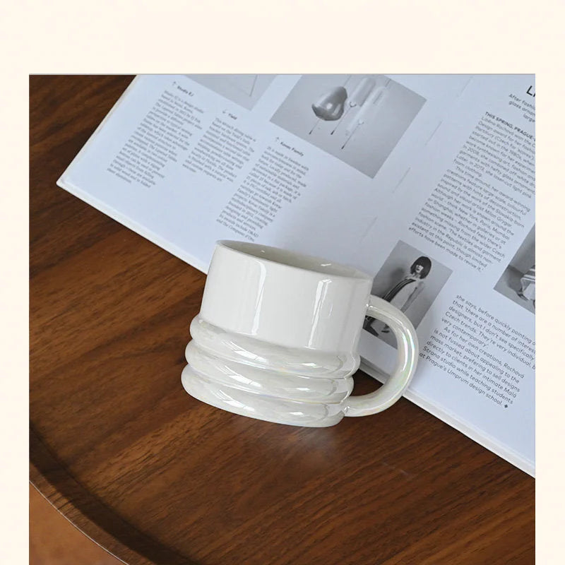 An iridescent white chunky ribbed ceramic mug tilted on its side on an open book - RoomDen.