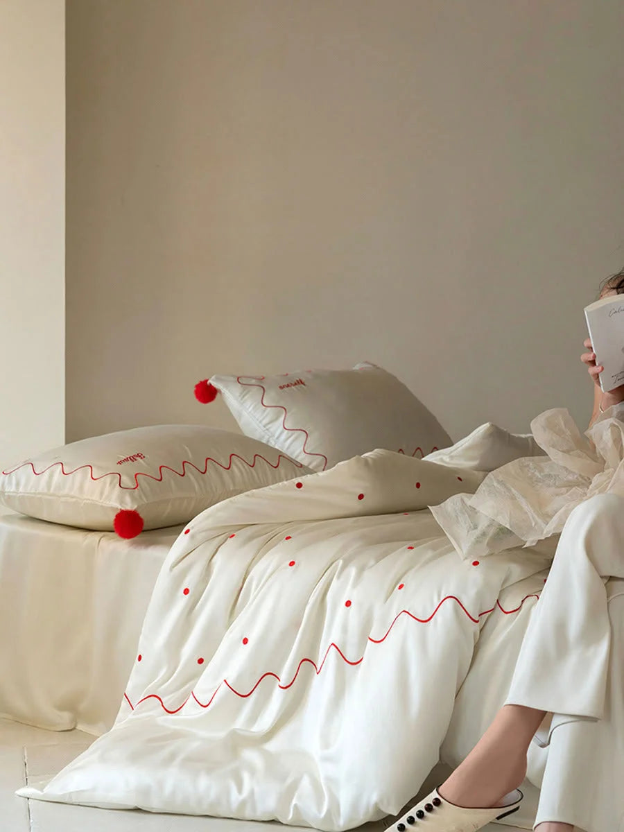 A person reading a book while relaxing on the Creamy White & Red silky embroidered Tencel bedding set. - RoomDen