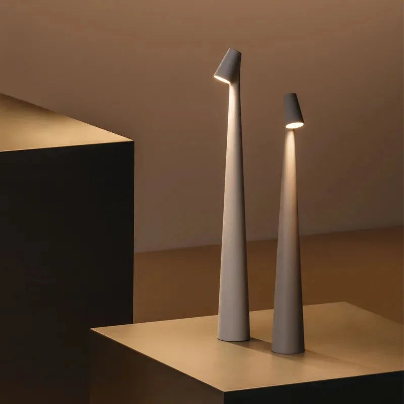 Two sculptural cordless accent lamps in taupe grey, one tall and one short, casting a warm glow in a minimalist setting - RoomDen.