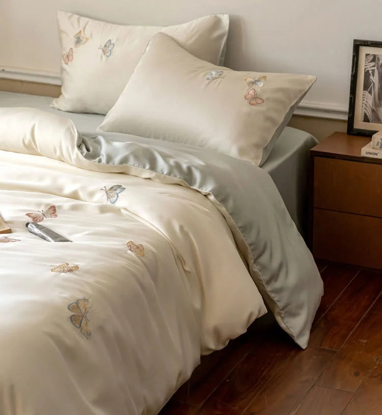 Close-up on the corner of the bed, highlighting the texture of the Tencel fabric and embroidered butterflies.