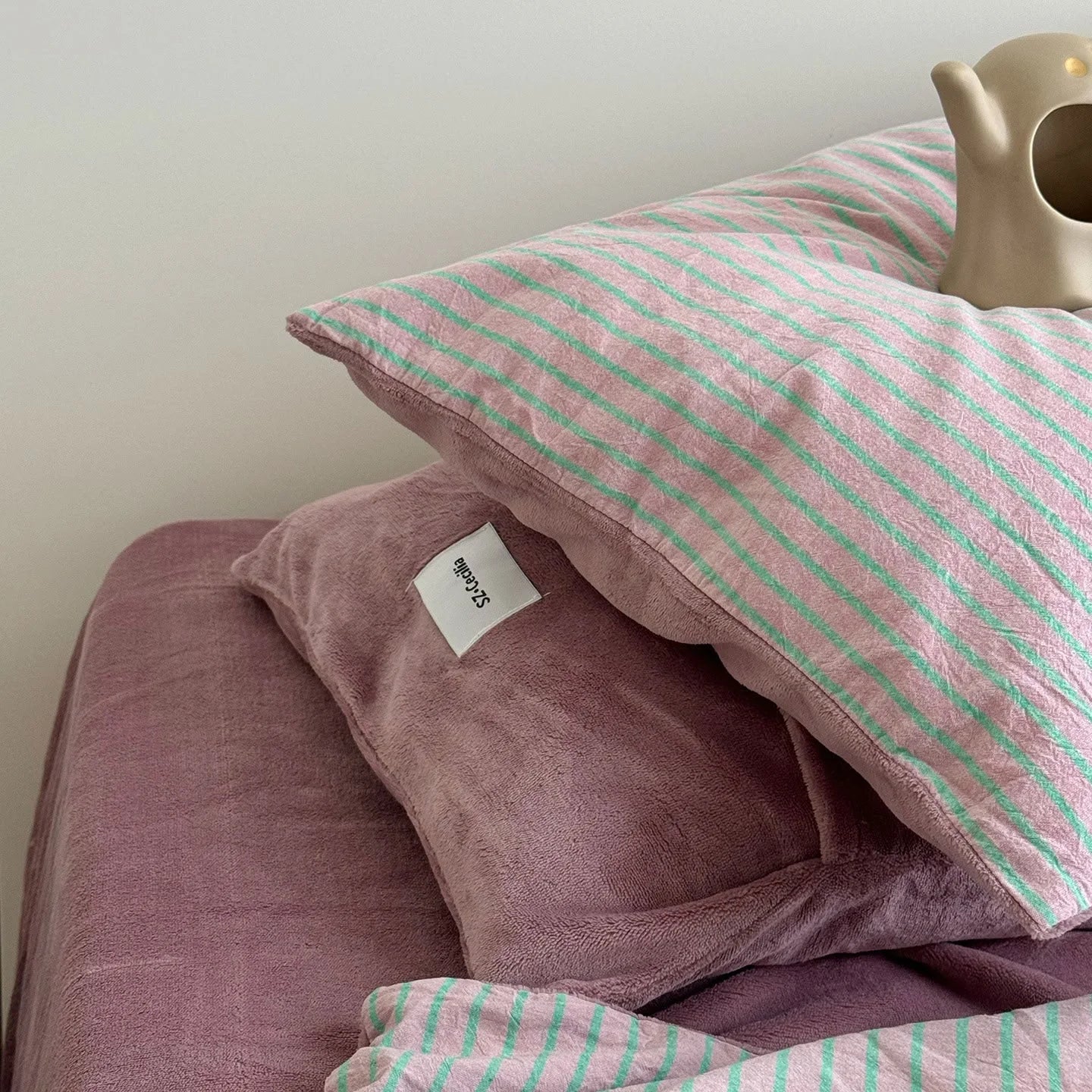 Detail shot of the pink fleece and mint striped pillowcases stacked together.