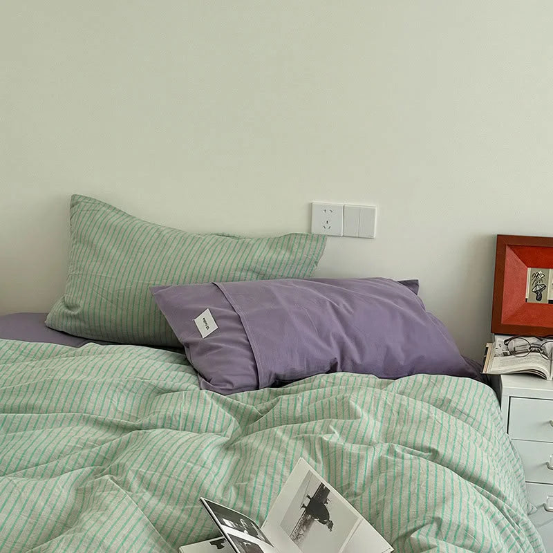 A bed dressed in the Mint & Lavender Striped Washed Cotton Bedding Set, with a solid lavender pillowcase visible - RoomDen.