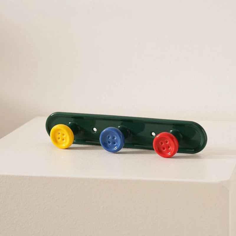 Green 3-hook button ceramic wall rack with colorful buttons on a white surface. - RoomDen