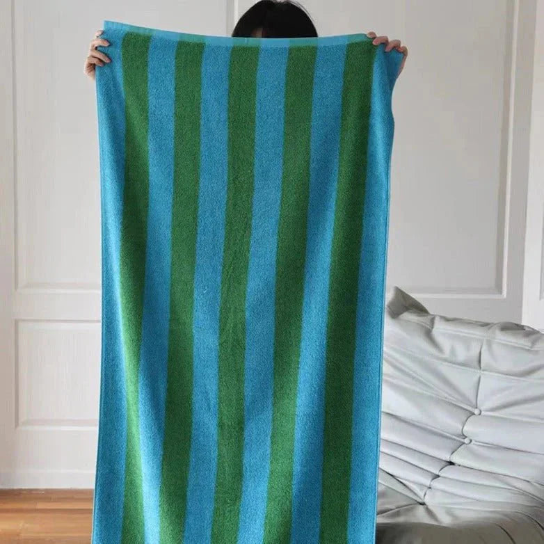 A person holding up a large blue and green bold striped cotton bath towel, showcasing its full size. - RoomDen