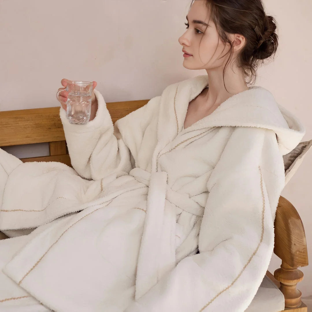 Model relaxing on a wooden bench in a creamy white plush hooded pajama set, holding a glass of water - RoomDen.