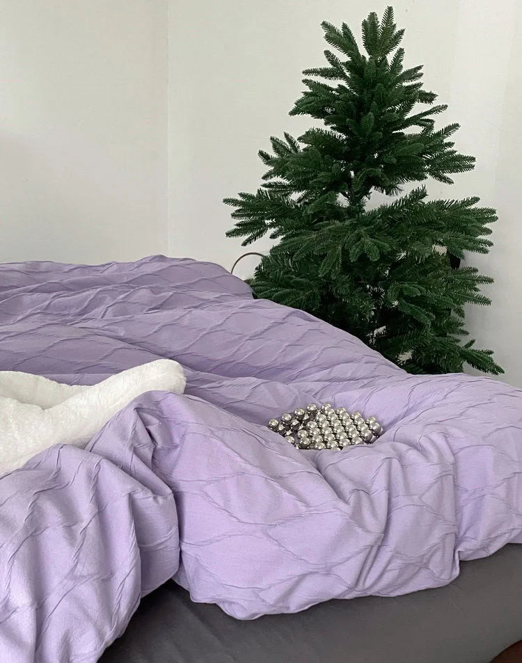 Detail shot focusing on the soft folds and crinkled texture of the lavender duvet cover next to a small pine tree.