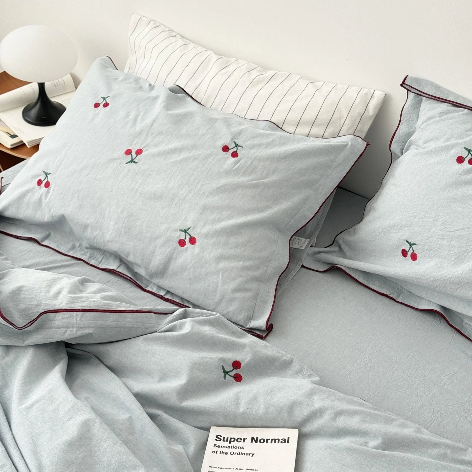 Close-up of the dusty blue pillowcases with cherry embroidery, styled with a modern lamp and books.