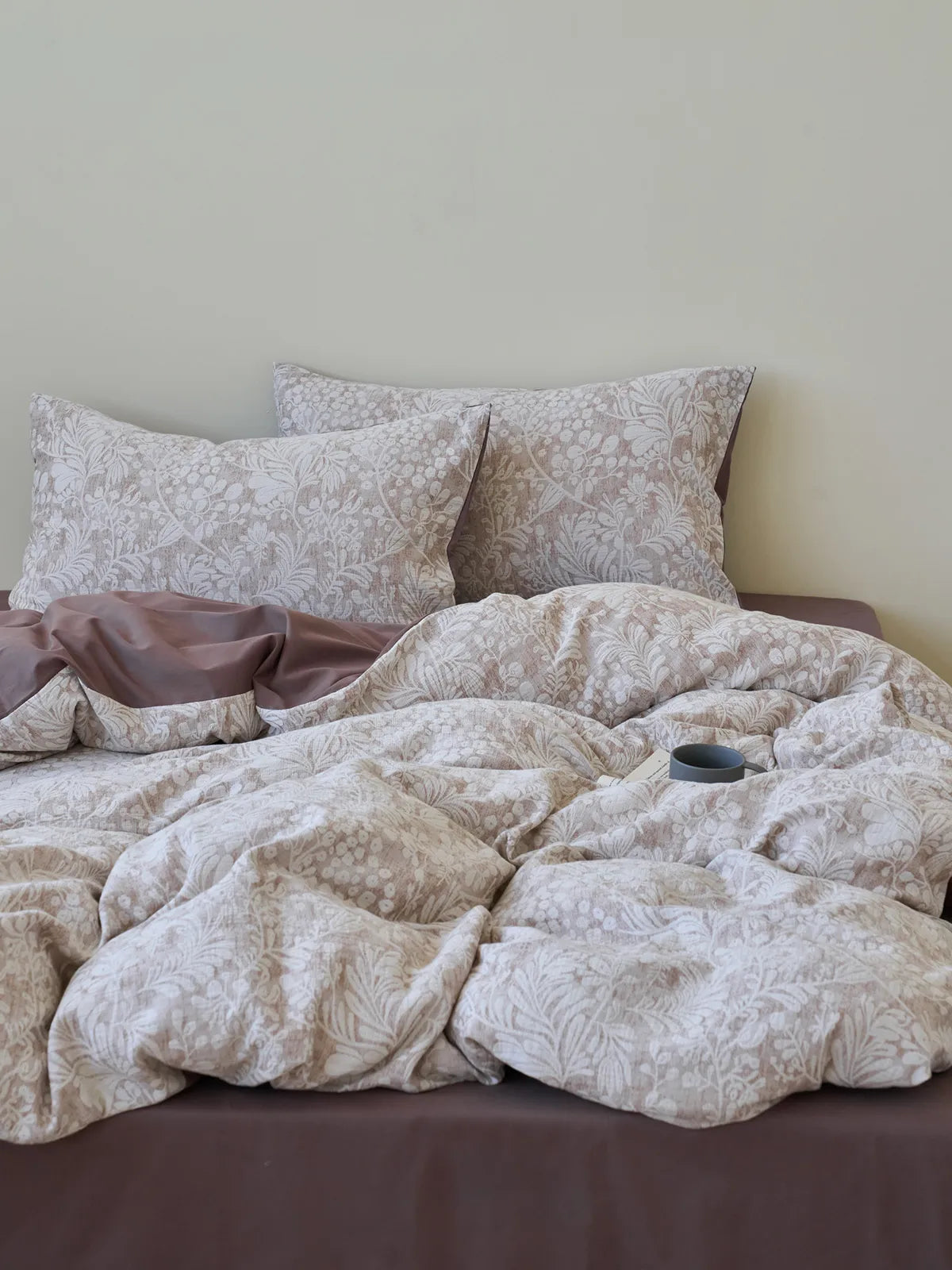 Full view of the bed dressed in the mocha brown and cream botanical print bedding set against a neutral wall, creating a serene and rustic atmosphere. - RoomDen