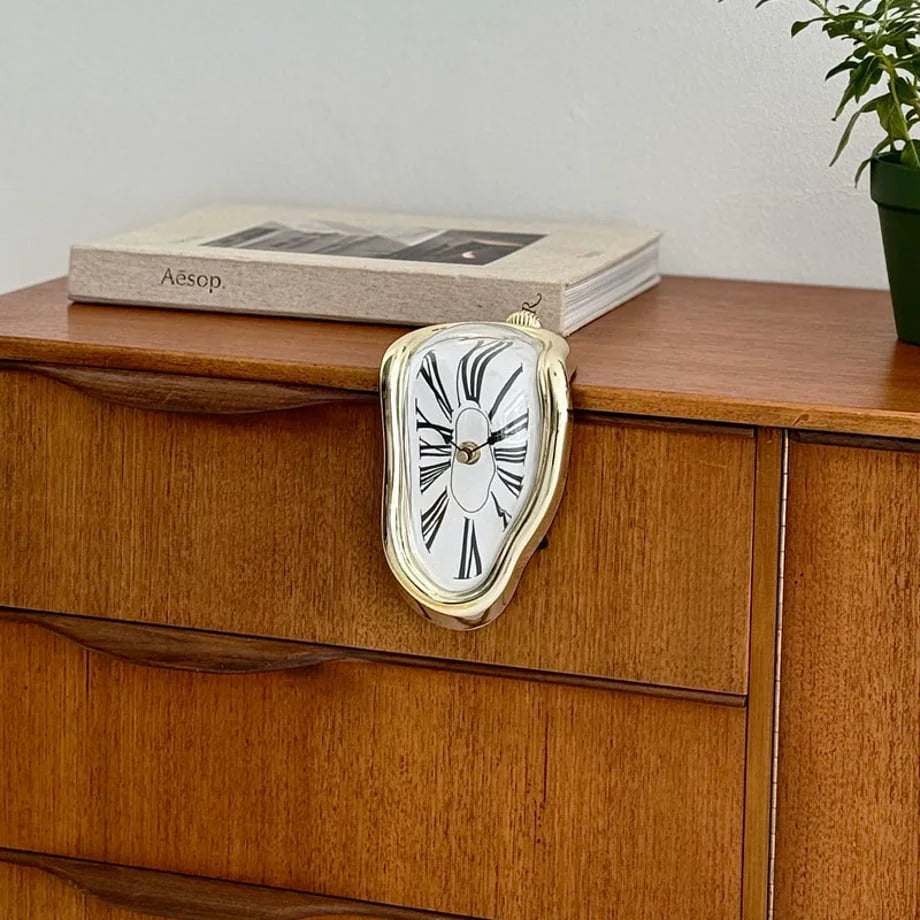 Lifestyle image of the gold melting clock adding a touch of surrealism to a wooden dresser.