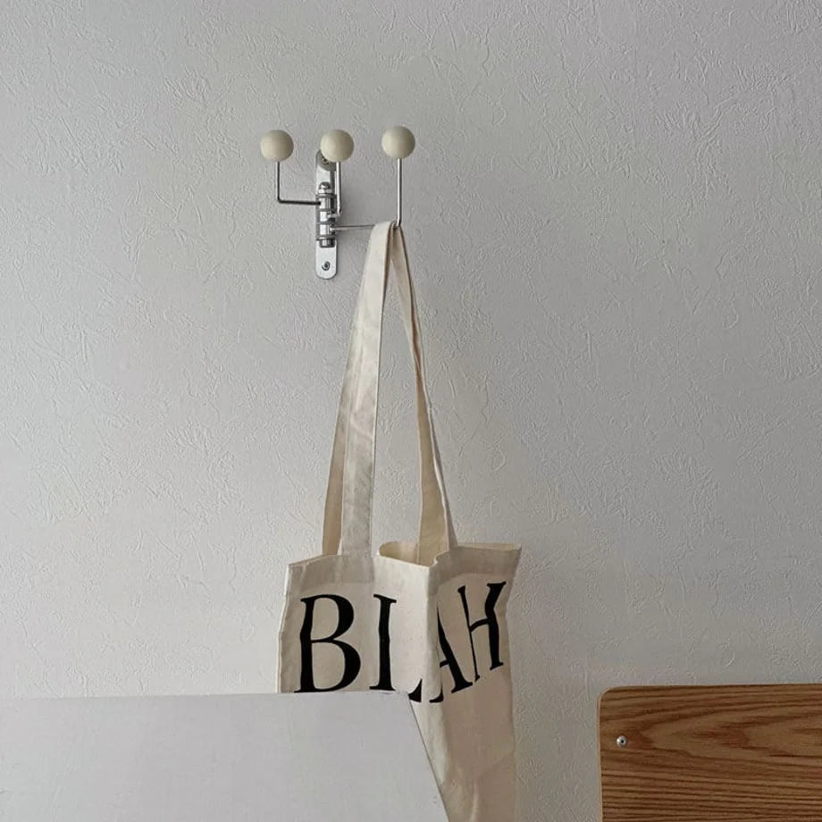 The Cream Ball-End Swivel Metal Wall Hook holding a 'BLAH' tote bag in a bright room - RoomDen.