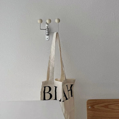 The Cream Ball-End Swivel Metal Wall Hook holding a 'BLAH' tote bag in a bright room - RoomDen.