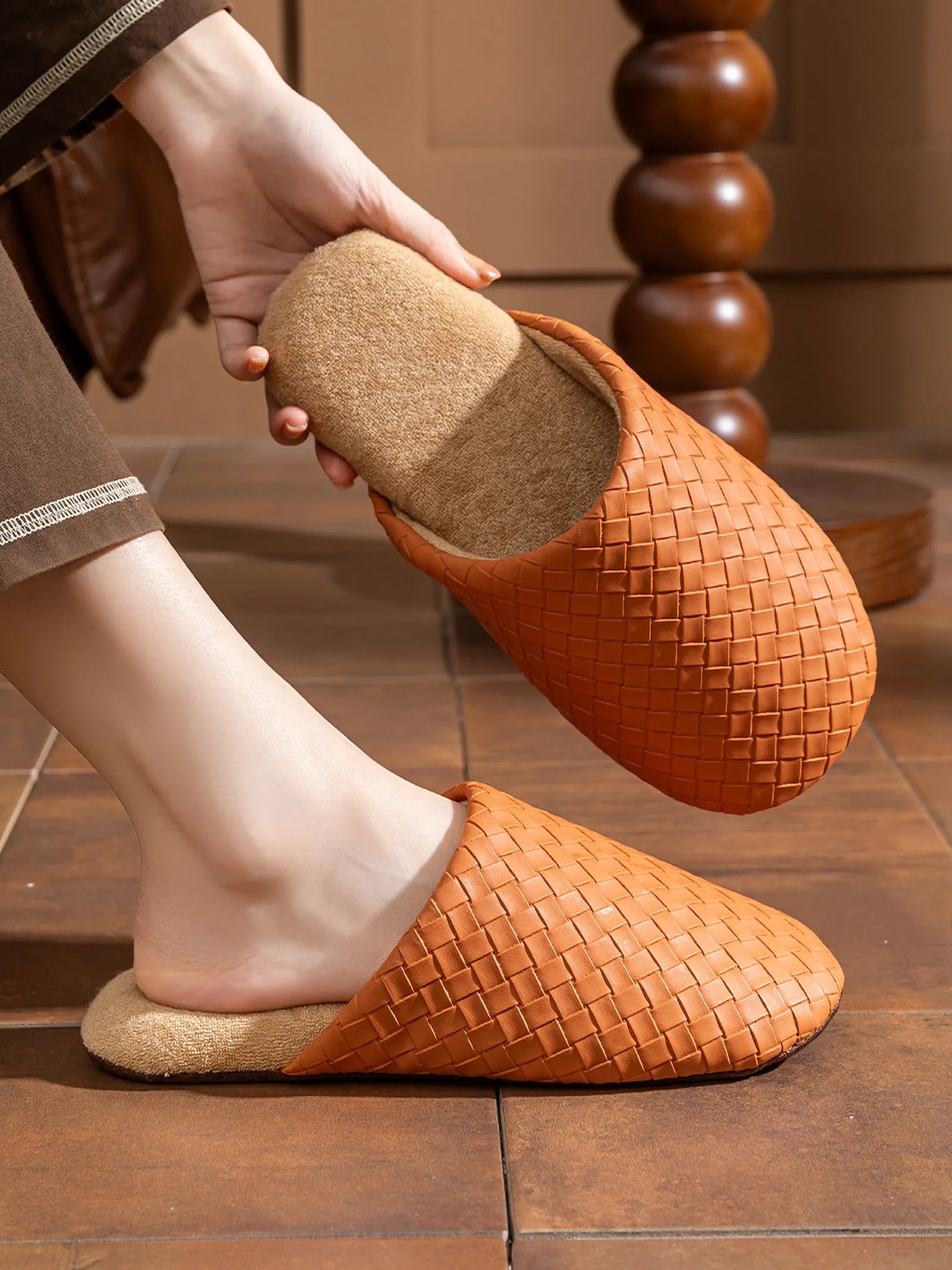 Model holding a brown woven slipper showing the fluffy interior lining
