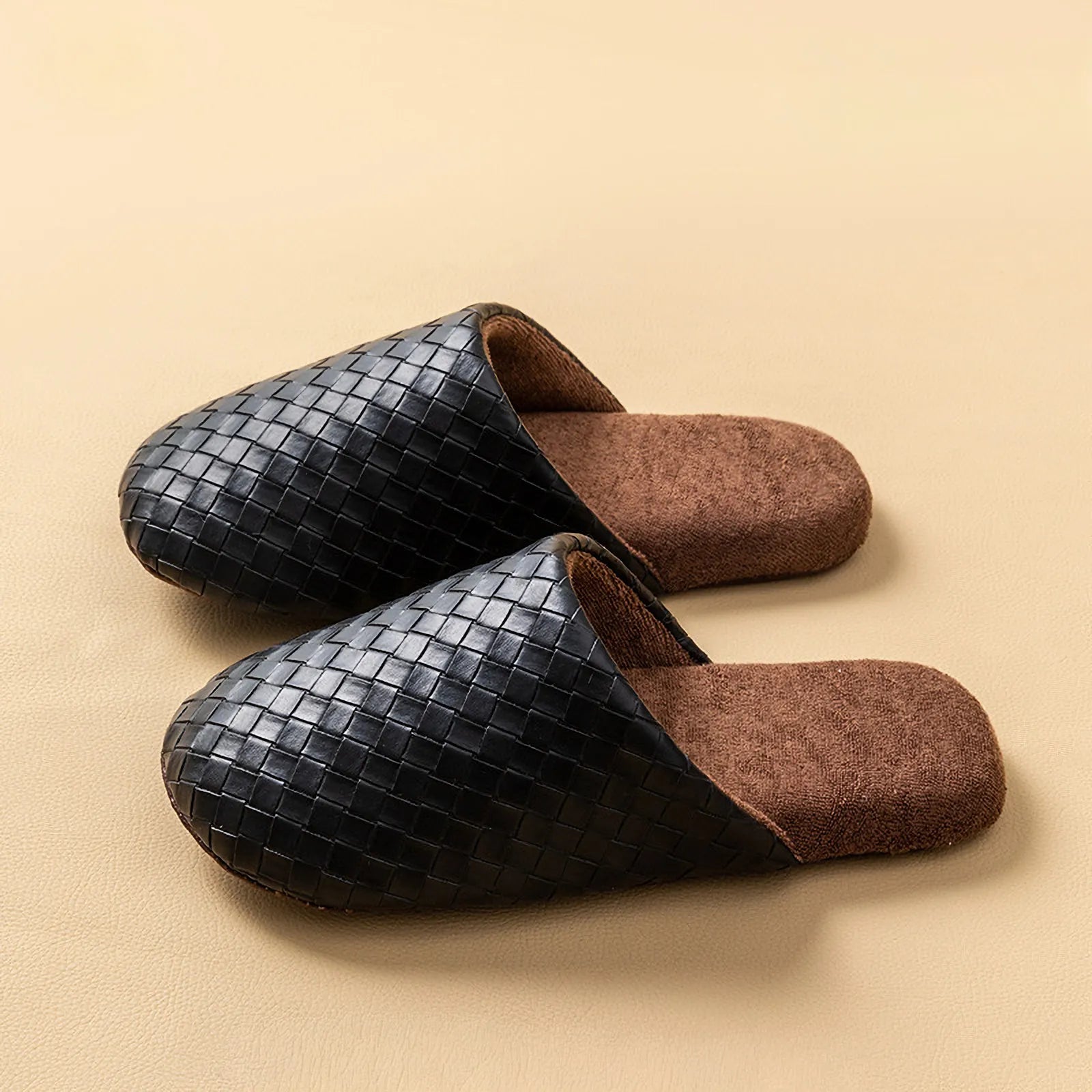 Pair of black woven texture house slippers on a beige surface