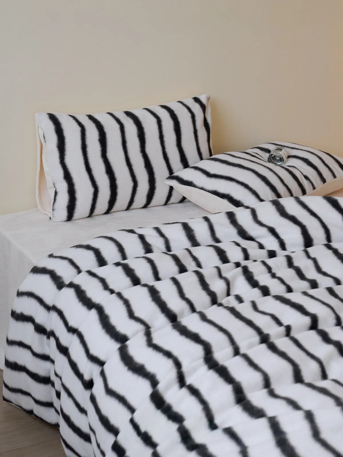 Plush black and white wavy striped flannel fleece bedding set on a bed against a beige wall - RoomDen.