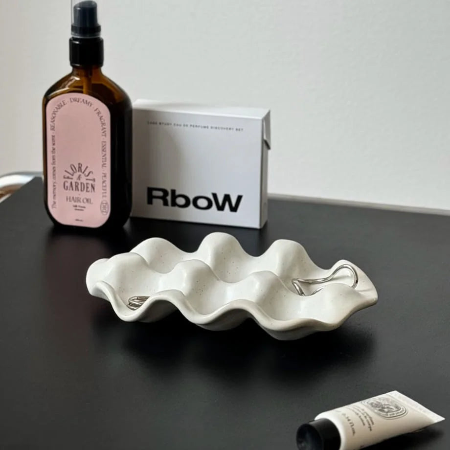 Angled view of the White Speckled Wavy Ceramic Jewelry Dish on a modern black desk.