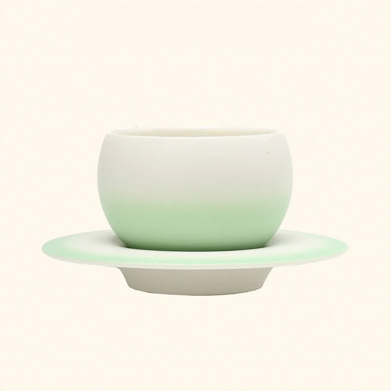 The Mint Green Ombre Ceramic Cup displayed on its matching Saturn-ring saucer. - RoomDen
