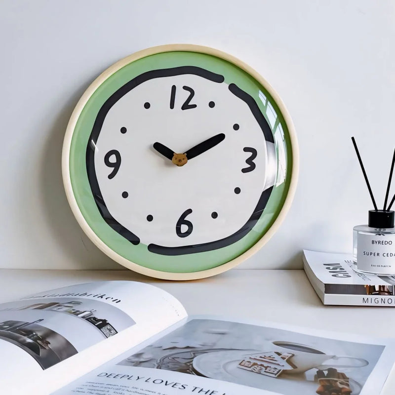 Close-up of the Green Whimsical Doodle Style Wall Clock resting on a desk beside a small stack of books, positioned at a working eyeline - RoomDen.