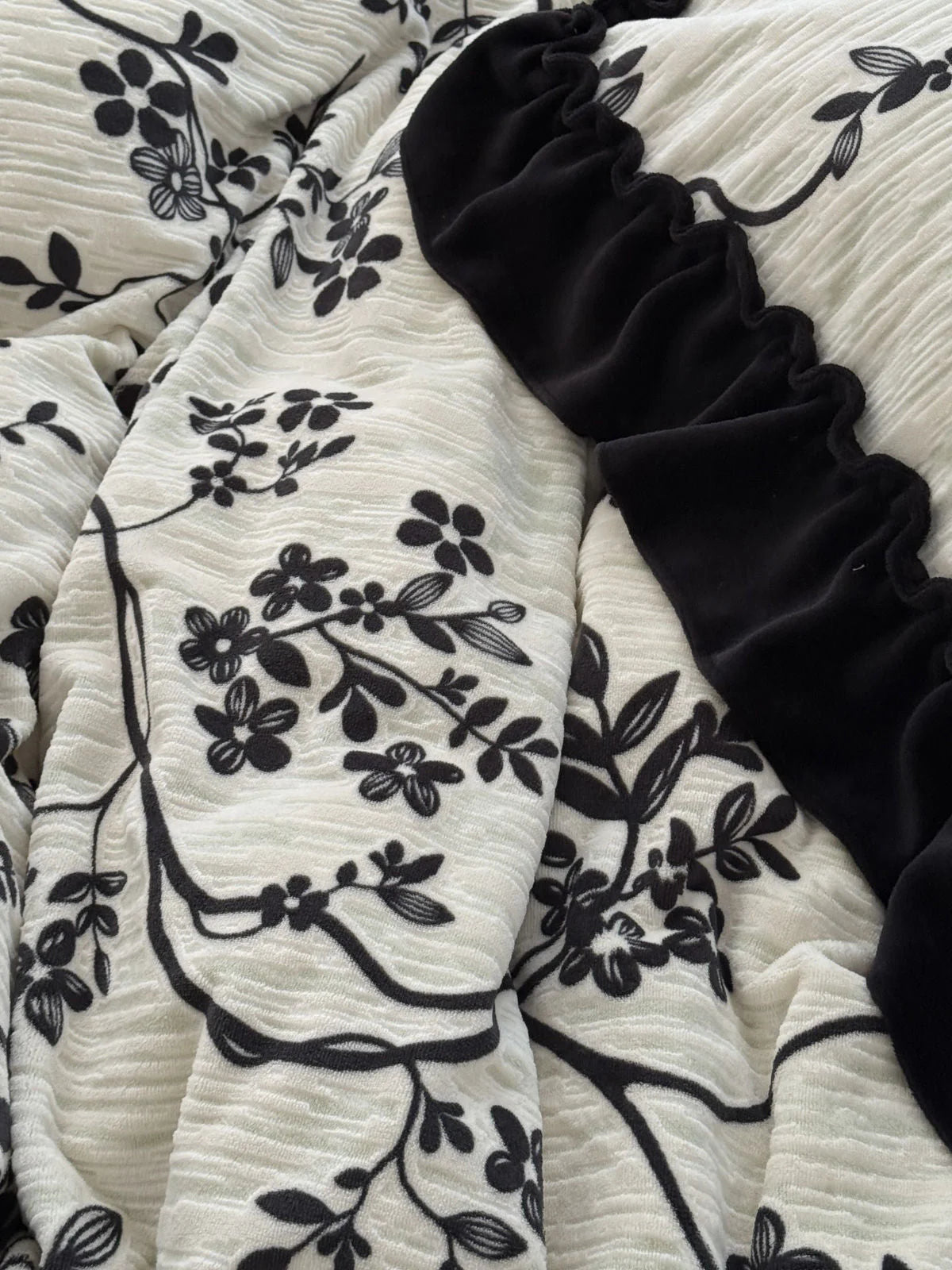 A macro shot of the washed cotton fabric, showing the intricate black vine pattern and the soft folds of the black ruffle detail - RoomDen.