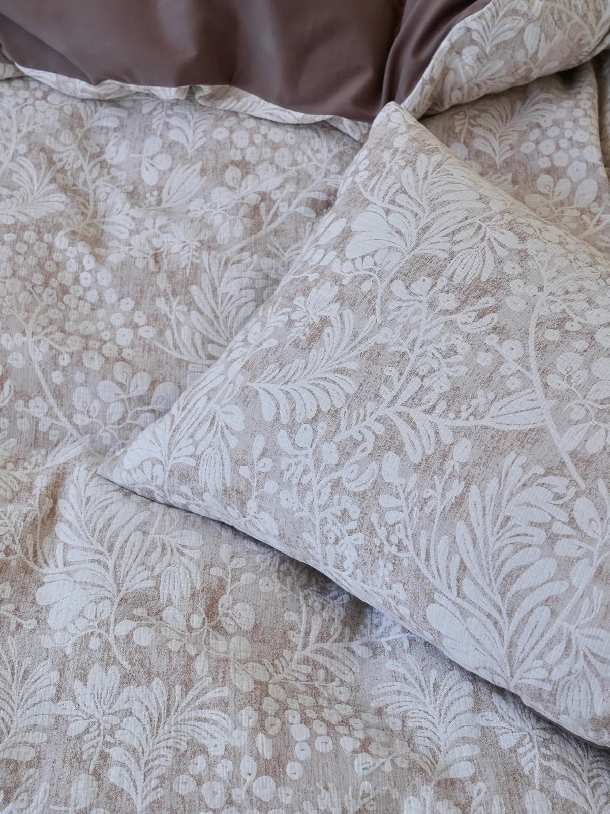 Detailed shot of the corner of a pillowcase, highlighting the intricate white and brown floral and berry pattern on the textured washed cotton fabric. - RoomDen