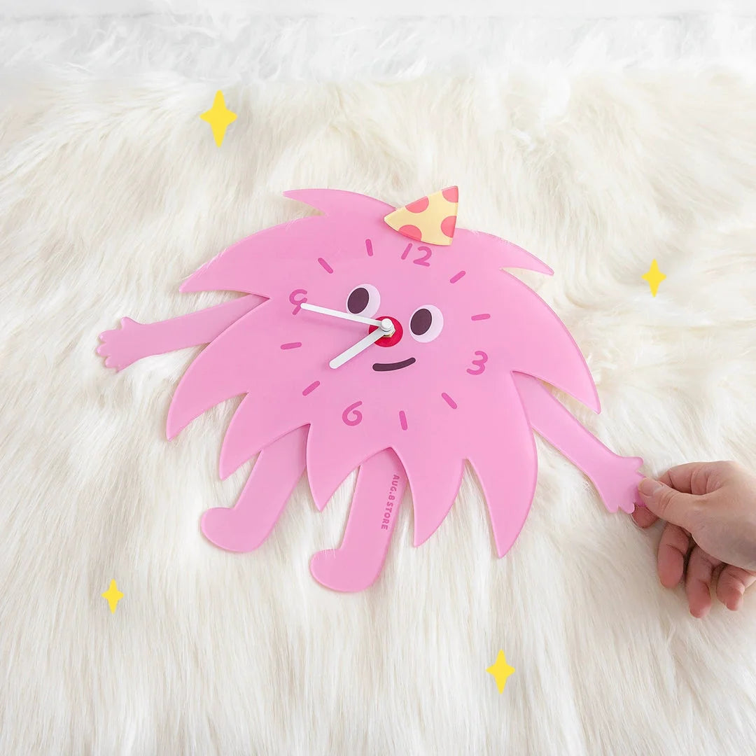 Close-up of the pink Party Monster Acrylic Clock resting on a fluffy white rug, showing its smooth texture.