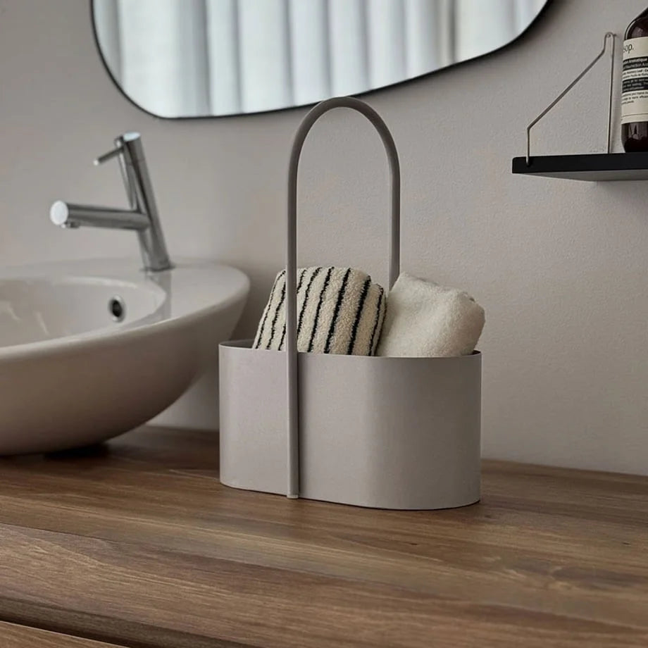 Lifestyle scene of the metal storage caddy organizing towels on a wooden bathroom counter. - RoomDen