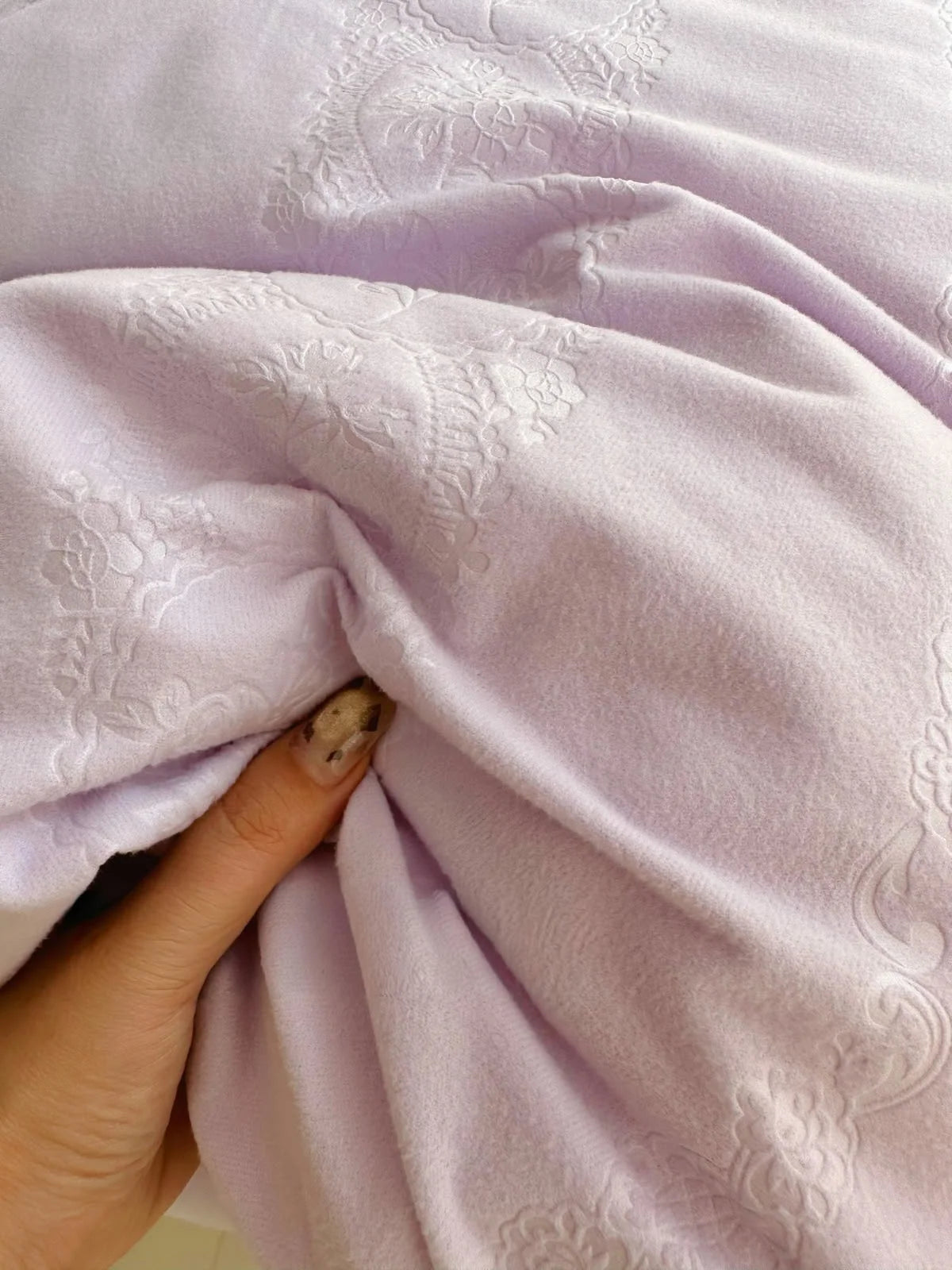 A hand touching the soft, plush velvet fabric of the lavender bedding, showing the texture. - RoomDen