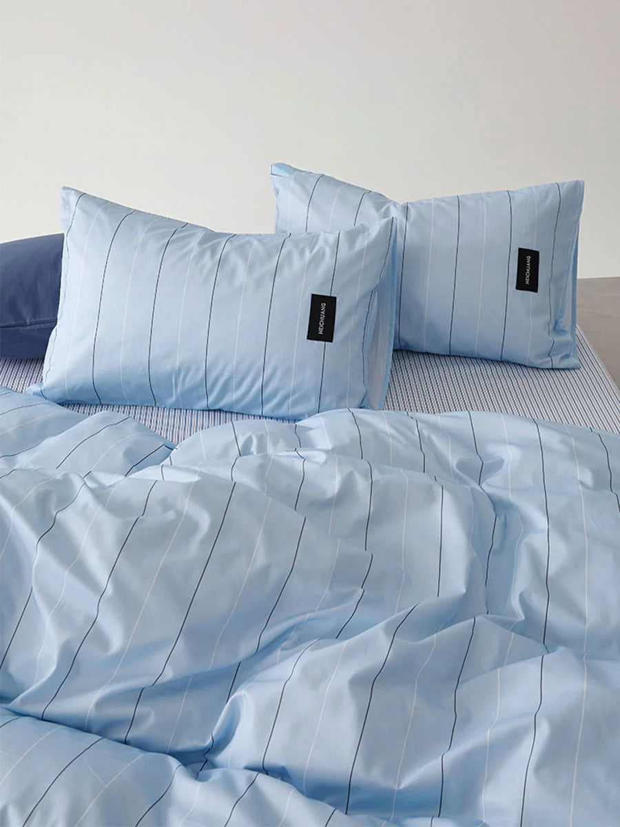 Close-up view of the Sky Blue Pinstripe pillowcases with the RoomDen label visible on a neatly made bed - RoomDen.