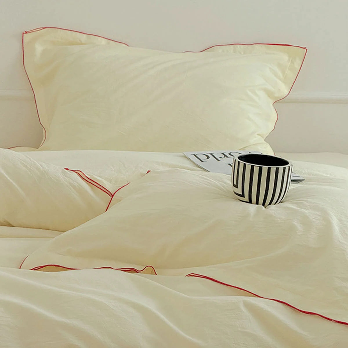 Close-up of the buttercream washed cotton bedding set with red ruffle trim, featuring a striped mug on a book.