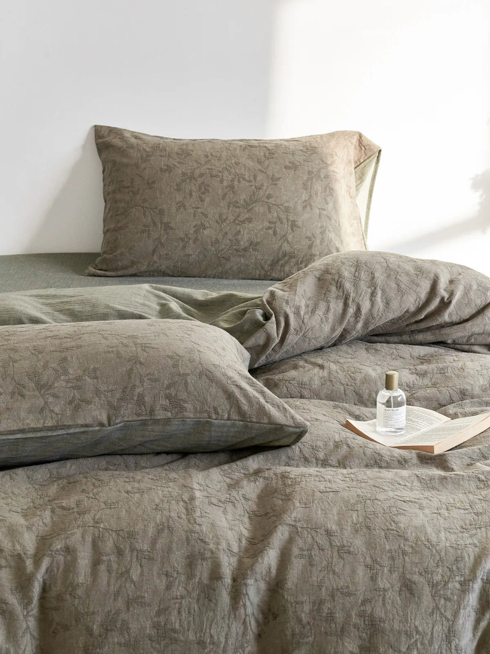 Close-up of Textured Botanical Washed Cotton Bedding Set in an earthy green color, showing the crinkled fabric and leaf pattern - RoomDen.