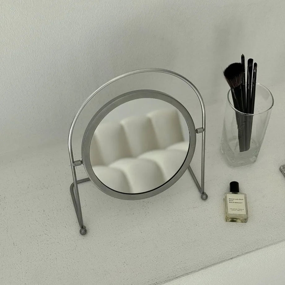 The metal makeup mirror reflecting a white sofa, showcasing its clear reflective surface. - RoomDen
