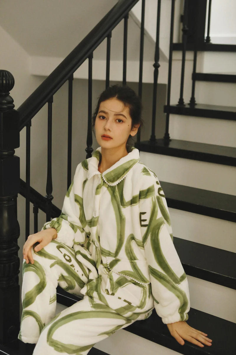 Model sitting on black stairs wearing the cozy green and white graffiti print flannel fleece pajamas - RoomDen.