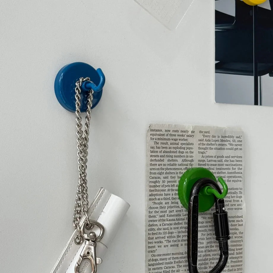 Close-up of a blue magnetic metal hook holding a white pouch with a silver chain on a metal surface - RoomDen