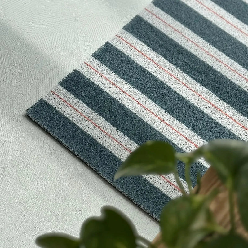 Green and white striped PVC coil rug with red pinstripe detail on a concrete floor - RoomDen