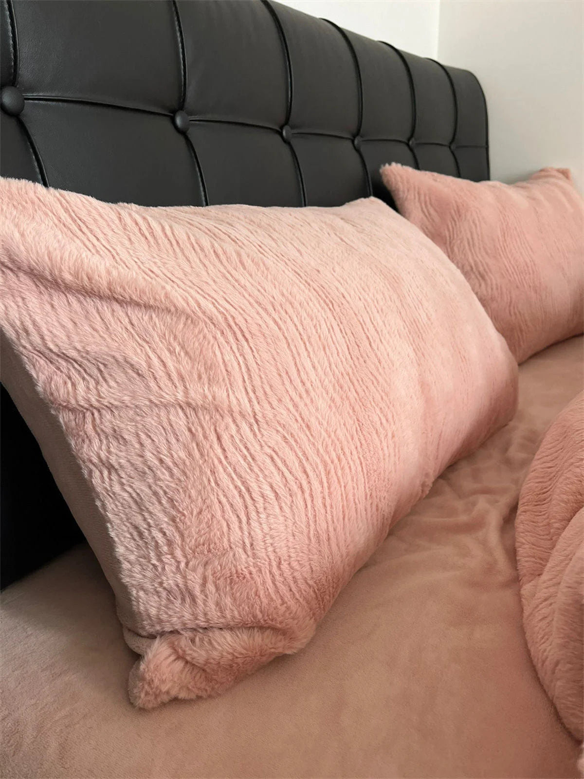 Detailed view of the fuzzy texture on a Blush Pink flannel fleece pillowcase against a black tufted headboard. - RoomDen