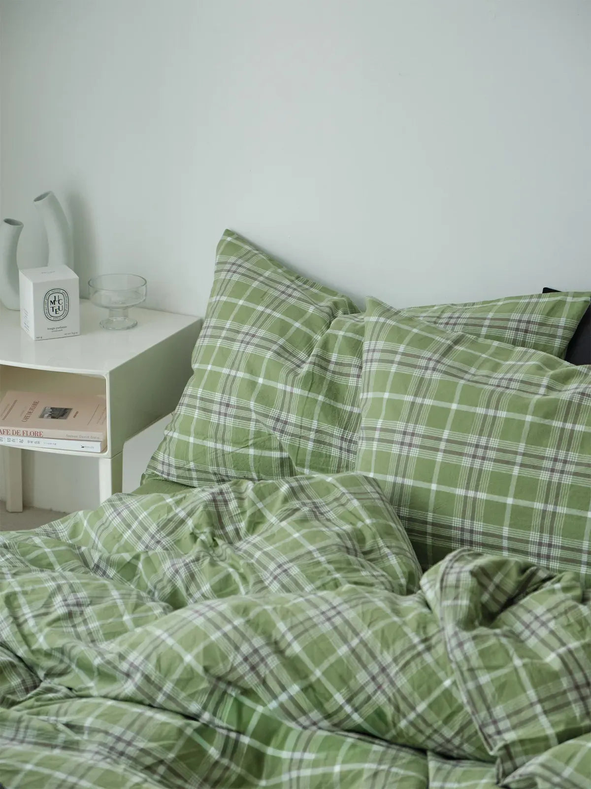 The green plaid bedding set in a serene bedroom setting, emphasizing its calming and cozy aesthetic next to a modern white nightstand. - RoomDen