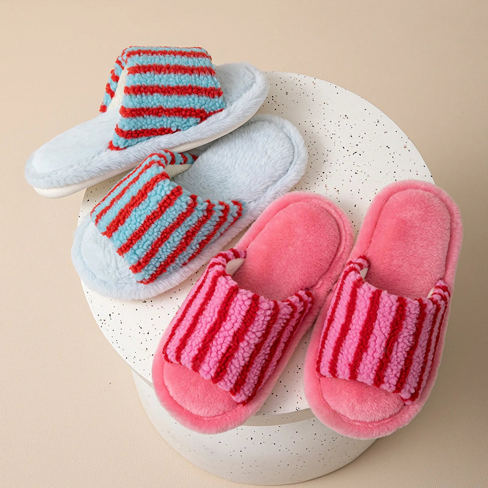 RoomDen fuzzy house slippers in Blue/Red and Pink/Red stripes on a speckled terrazzo table