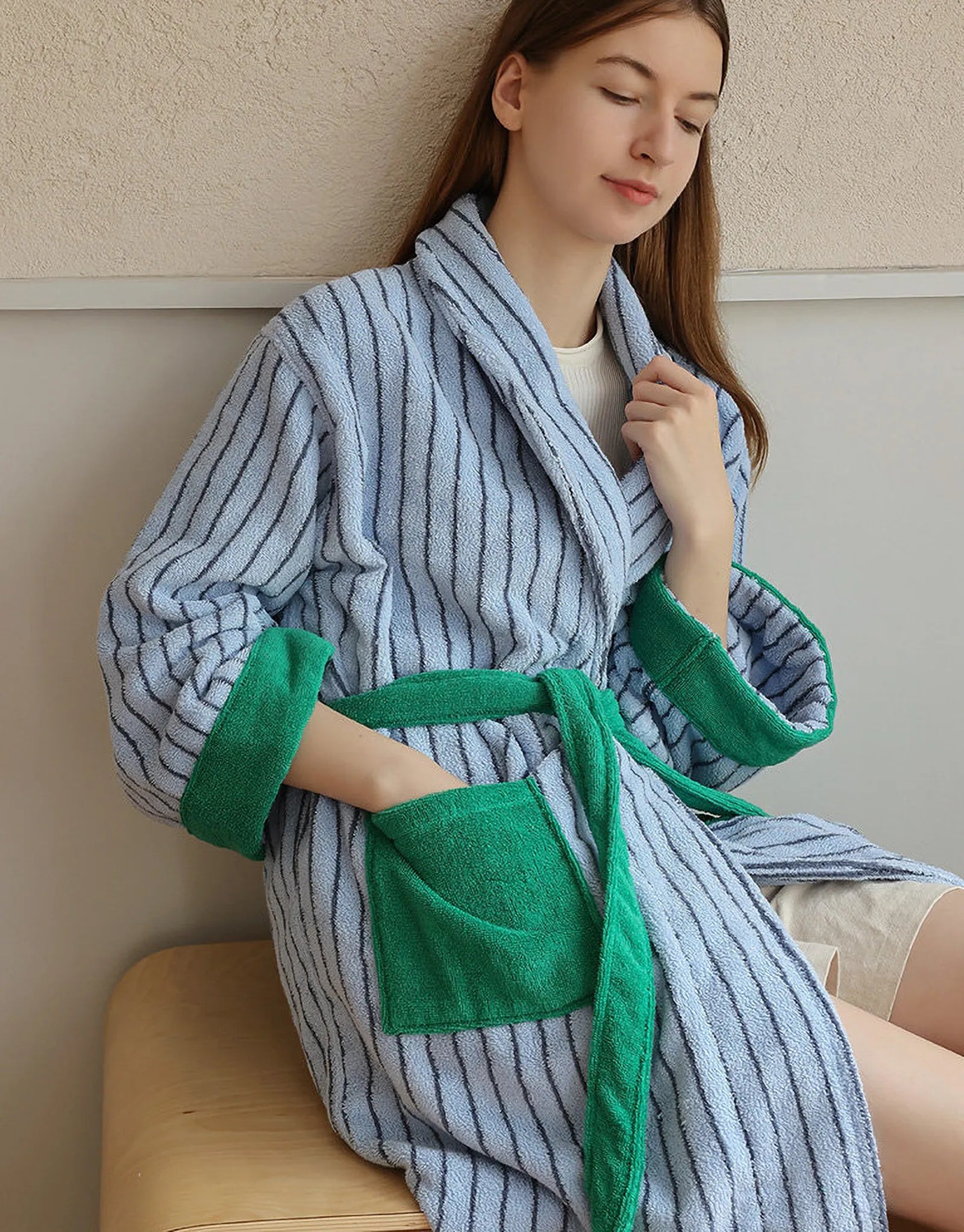Woman adjusting the shawl collar of the blue striped bathrobe with green accents.