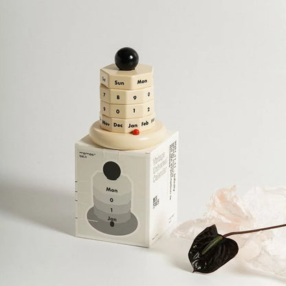 The beige and black perpetual calendar shown next to its minimalist white packaging box. - RoomDen